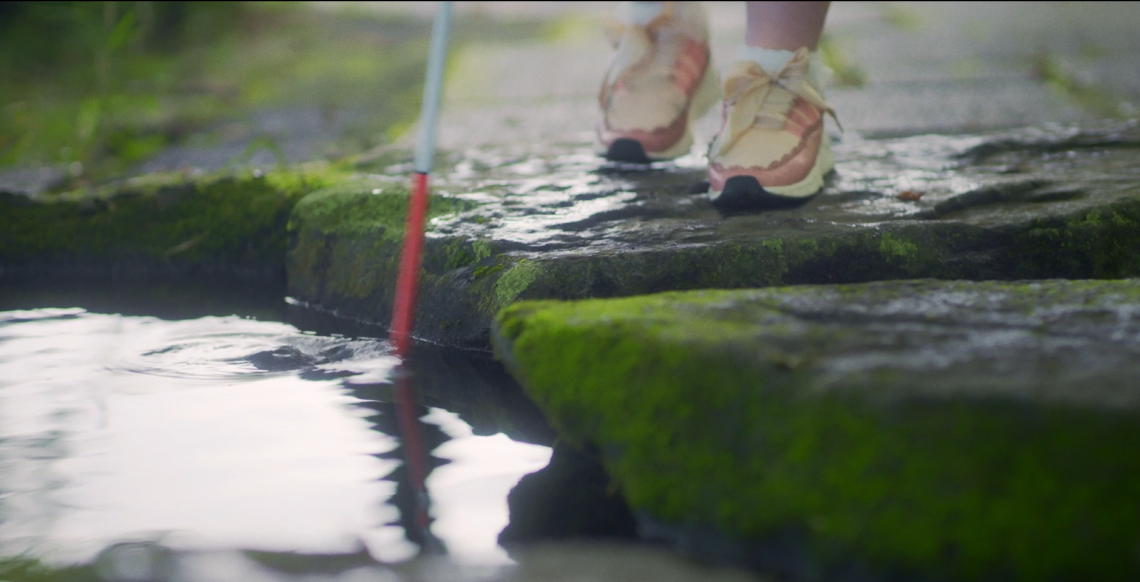 白杖を使って池の中の飛び石を歩く