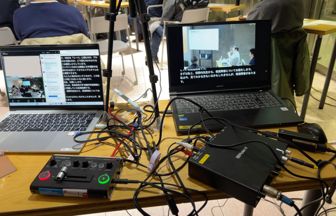 文字通訳・画面合成で使用した機材。パソコン2台とオーディオミキサー・映像切替機などがケーブルとともに映っている。